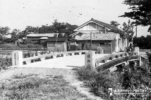 欄干に「稚鯉橋」と刻まれた橋がかかり、渡った先に小屋や瓦屋根の家屋が建っている。